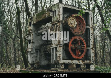 An old abandoned sheet metal working machine in the forest. Iron and steel production. Industrial history machine. Red gears. Stock Photo