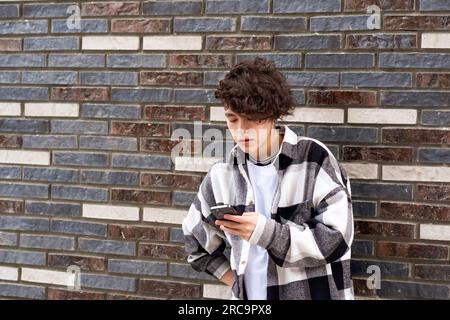 young man reading message on phone against a brick wall Stock Photo