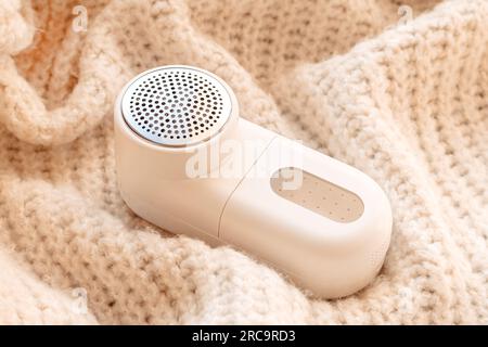 Modern white fabric shaver device and light woolen sweater, closeup Stock Photo