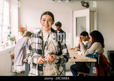 Portrait of smiling female teacher wearing plaid shirt with students in background at carpentry class Stock Photo