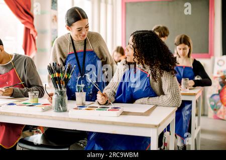 Smiling female teacher assisting teenage student during art class at high school Stock Photo