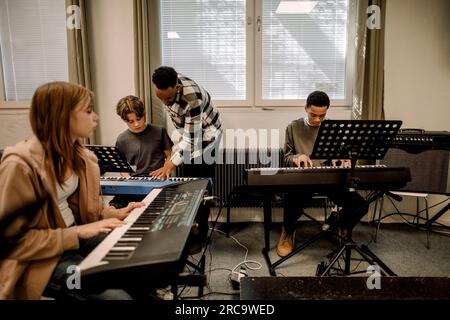 Teacher assisting teenage students during piano class at high school Stock Photo