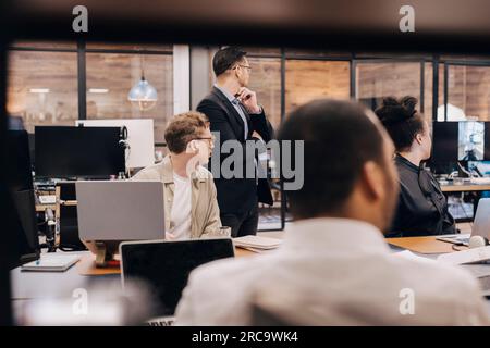 Business manager and colleagues looking at computer monitor during meeting in office Stock Photo