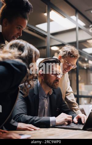 Mature male manager discussing over laptop with colleagues at office Stock Photo