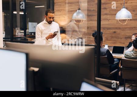 Businessman using smart phone standing at illuminated creative office Stock Photo