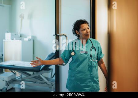 Female doctor wearing scrubs gesturing at doorway in hospital Stock Photo
