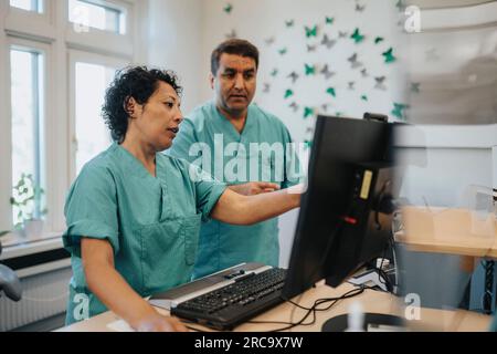 Male and female healthcare workers discussing over computer at reception desk in hospital Stock Photo