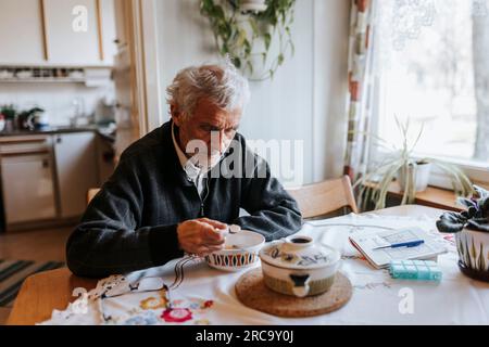 Senior man eating breakfast while sitting at dining table in home Stock Photo