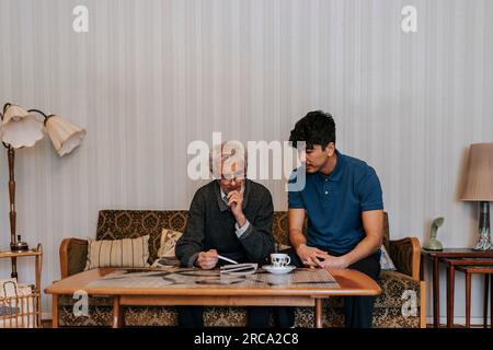Senior man discussing with male caregiver sitting on sofa at home Stock Photo
