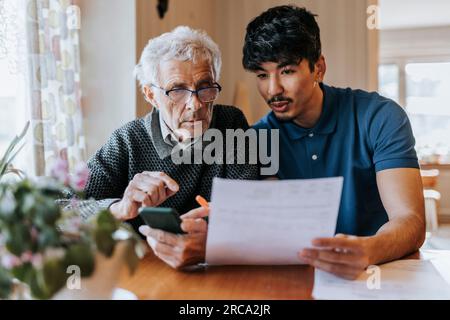 Male care assistant explaining medical reports to senior man at home Stock Photo