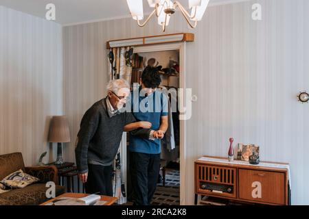 Male caregiver holding hands of senior man while walking at home Stock Photo