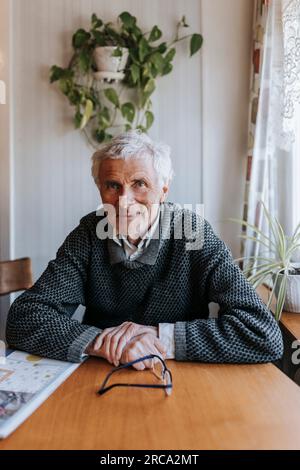 Smiling senior man sitting at dining table in home Stock Photo