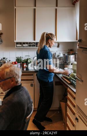 Side view of female healthcare worker preparing coffee while standing in kitchen at home Stock Photo