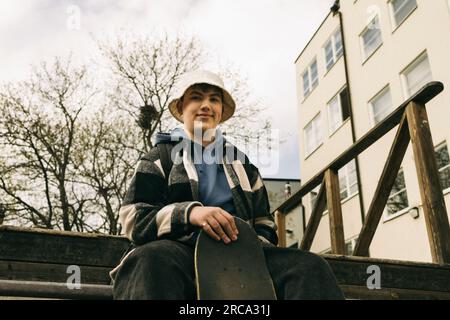 Low angle view of smiling young man wearing bucket hat while sitting on steps Stock Photo