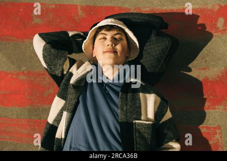 Directly above view of young man lying on floor with eyes closed during sunny day Stock Photo