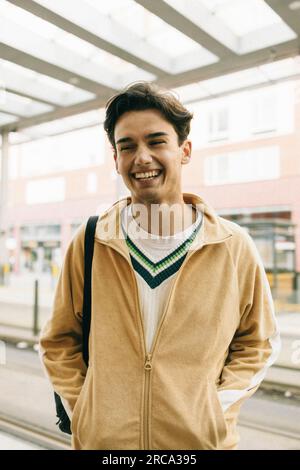 Happy young man with hands in pockets while standing at train station Stock Photo