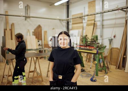 Portrait of female carpenter standing with hands in pockets at workshop Stock Photo