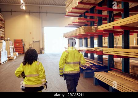 Rear view of female workers in protective workwear walking by rack in lumber industry Stock Photo