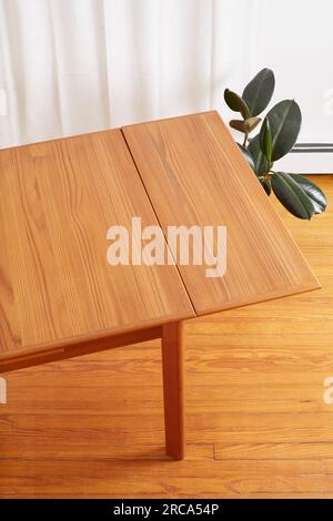 Vintage draw-leaf dining room table. Mid-century modern teak furniture. Interior photograph with luxurious long white curtains and houseplants. Stock Photo