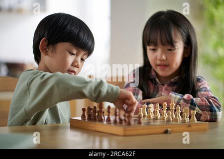 two asian children brother and sister sitting at table at home playing chess Stock Photo