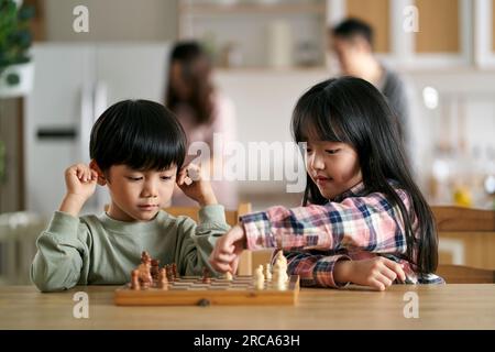 two asian children brother and sister sitting at table at home playing chess Stock Photo