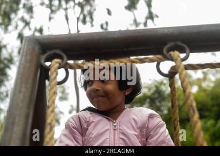 A small girl is climbing up a rope in the park. She is focused and determined, and her face is full of determination. Stock Photo