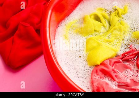 Plastic basin with dirty laundry, water and foam on pink background Stock Photo