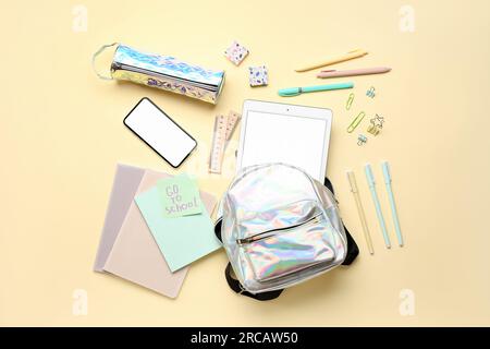 Sticky note with text GO TO SCHOOL, backpack, stationery and gadgets on yellow background Stock Photo