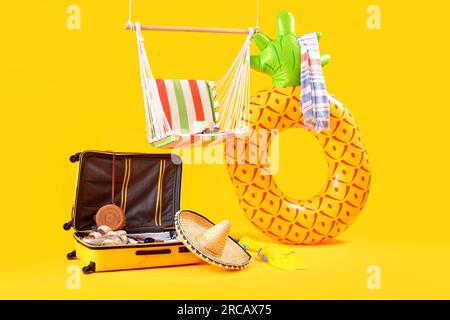 Hanging hammock with suitcase and beach accessories on yellow background. Travel concept Stock Photo