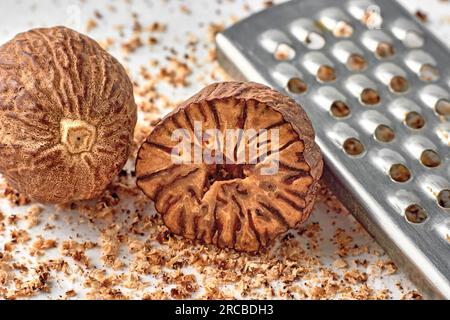 Half and whole nutmeg and metal grater on background of scattered grated nut powder. Stock Photo