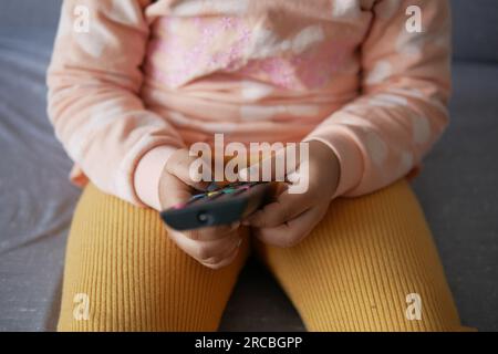 close up of child hand holding tv remote sitting on sofa  Stock Photo