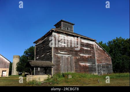 Unique barn structure has cupola on top.  Barn at one time was painted white, and you can see the weathered remains at the top.  Stone water well sits Stock Photo