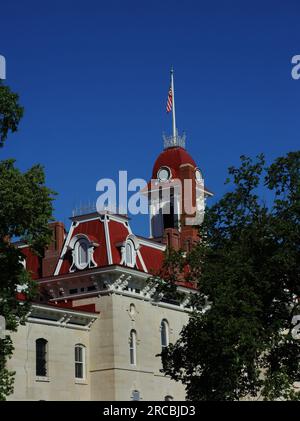 Beautiful courthouse in Cottonwood Falls, Kansas has burgundy roof, trimmed in white.  Flat pole tops dormer style turret. Stock Photo