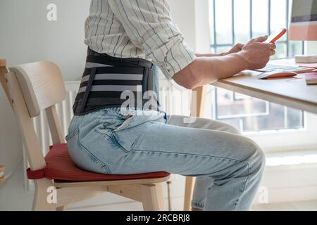 Man freelancer wearing back support belt working remotely from home Stock Photo