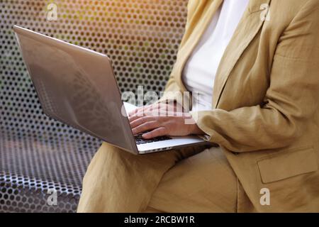Work life balance. Unrecognisable adult woman works, types on laptop on bench outdoors. Freelance social distance work, e-learning, connection, creati Stock Photo