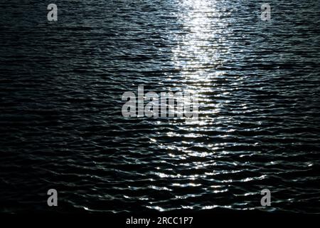 Rippled water surface with sun path reflections, dark tone image with high contrast. Stock Photo