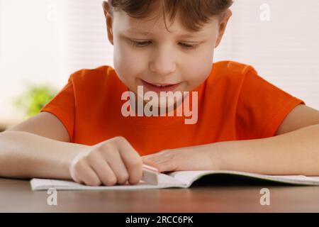Little boy erasing mistake in his notebook at wooden desk Stock Photo