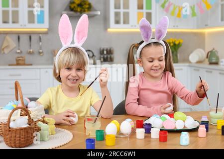 Children painting Easter eggs at table in kitchen Stock Photo