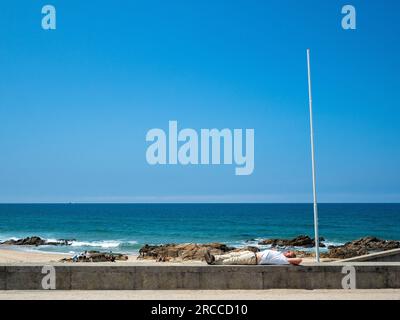 June 14, 2023, Praia do Aterro, Matoshinos, Portugal: A man is seen resting on a wall in front of the sea. The Coastal Route of the Portuguese Camino is a beautiful alternative walk to the Central Route. The total distance of the route is 280 km. It starts in Porto and follows the coast till Redondela in Spain where it merges with the Central Route. About 30% of pilgrims who complete the Portuguese Camino walk the Coastal Way. The Portuguese Camino is getting more and more popular, and many pilgrims choose this route as an alternative to the Camino Frances. The Coastal Route of the Portuguese Stock Photo