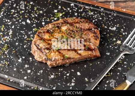Grilled ribeye steak with rosemary and thyme on stone cutting board Stock Photo