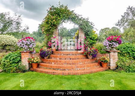 An ornate iron garden gate and steps decorated with tubs of colourful petunia flowers Stock Photo