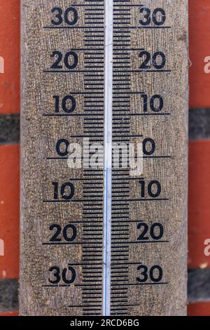 A close up portrait of a thermometer gauge showing a temperature measurement of zero degrees celcius. The intstrument is hanging on a brick wall. Stock Photo