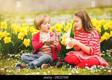 Cute little kids, big sister and small brother, with chocolate Easter bunnies celebrating traditional feast. Family, holiday, spring , carefree childh Stock Photo