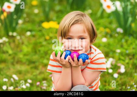 Adorable little blond boy playing with colorful easter eggs in the park, egg hunt Stock Photo