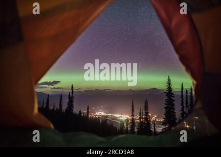 View of aurora, mountain town and forest from inside camping tent Stock Photo