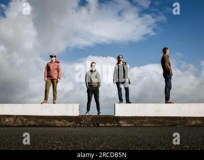 four friends stand on a white wall looking in different directions Stock Photo