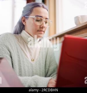 University student with  purple hair and eyebrows on her laptop Stock Photo