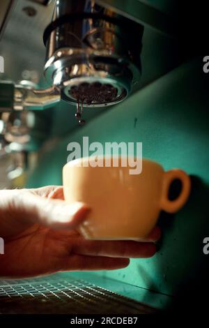 caucasian male hand holding orange cup below the of espresso coffee machine Stock Photo