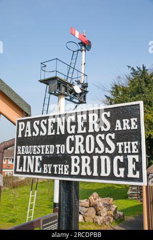 Vintage health and safety public notice sign at UK heritage railway station advising that 'Passengers are requested to cross the line by the bridge'. Stock Photo