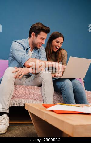 Vertical portrait of young couple watching the laptop screen, checking finances, planning budget or mortgage sitting at couch. Smiling husband showing on his wife's notebook a online shopping sale. High quality photo Stock Photo